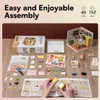 A flat lay of a miniature house kit with various components and instructions spread out on a wooden surface. A partially assembled miniature kitchen is shown in the upper right corner. Podgląd zdjęcia produktu