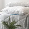 Two white quilted pillows are stacked on top of a white quilted comforter. A green plant is in the foreground. Produktbild-Vorschau