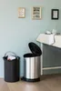 Two trash cans are shown in a room with framed pictures on the wall and a table covered with a tablecloth. Anteprima dell’immagine prodotto