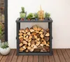A firewood rack with logs stored inside, placed on a wooden deck next to a white wall. Small potted plants and a decorative lantern are on top of the rack. Podgląd zdjęcia produktu