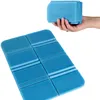 A hand holding a stack of folded blue seat cushions, with one cushion unfolded in the foreground. Produktbild-Vorschau