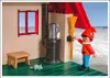 A Playmobil figure is standing next to a stove and broom inside a small structure, with a window showing a landscape. Produktbild-Vorschau