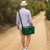 A man walks down a dirt path carrying a green cooler bag over his shoulder. Produktbild-Vorschau
