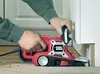 A person is using a belt sander to sand a wooden floor near a wall. Anteprima dell’immagine prodotto