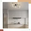 A modern kitchen with white cabinets, a stainless steel refrigerator, and a sleek black range hood. A contemporary square ceiling light fixture with integrated LED lighting is mounted on the white ceiling. Produktbild-Vorschau
