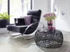 A modern living room scene with a black rocking chair, a laptop, a plant, and a round coffee table with a vase of flowers. Anteprima dell’immagine prodotto