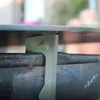 A close-up shot of a metal bracket with a flame logo, attached to the rim of a dark, weathered metal fire pit or grill. Produktbild-Vorschau