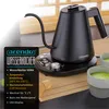 A black electric kettle with a gooseneck spout sits on its base, next to two cups of matcha tea and a bamboo whisk. Produktbild-Vorschau