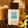 A perfume bottle is displayed with coffee beans, caramel candies, and vanilla flowers, suggesting a gourmand fragrance. Podgląd zdjęcia produktu