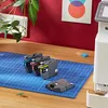 Printer ink cartridges are arranged on a blue cutting mat on a wooden desk, with a printer and a plant in the background. Voir les images du produit