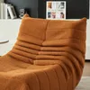 A close-up view of an orange textured sofa or armchair with a book and camera on a shelf in the background. Voir les images du produit