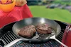 Steaks are being cooked in a pan on a grill outdoors. Voir les images du produit