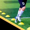 A person's legs and feet are shown training with soccer cones on a green field. Náhled obrázku produktu