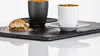 Two espresso cups with saucers and a cookie on a slate tray. Náhled obrázku produktu