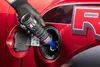 A gloved hand is pouring a liquid from a blue and silver can into a car's fuel tank. Produktbild-Vorschau