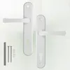 Two white door handles with keyhole plates and some screws and caps are arranged on a light background. Produktbild-Vorschau