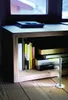 A small silver LED light is placed on a wooden floor in front of a wooden shelf unit filled with books, illuminating the floor. Podgląd zdjęcia produktu