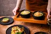 A person is serving a meal with soup and pasta on a wooden table. Náhľad obrázku produktu