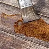 A paintbrush is applying oil to a wooden surface. Produktbild-Vorschau