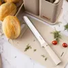 A kitchen set with knives and a cutting board, featuring bread rolls and herbs. Produktbild-Vorschau
