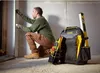 A construction worker is measuring a wall with a tape measure, with a tool backpack and level nearby. Voir les images du produit