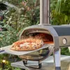A pizza oven is shown outdoors with a pizza being removed from it. Produktbild-Vorschau