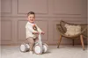 A young child is happily riding a balance bike in a room with decorative wall paneling and a woven chair. Náhľad obrázku produktu