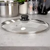 A close-up view of a glass pot lid with a black handle, resting on a speckled gray countertop. A large stainless steel pot is visible in the background. Produktbild-Vorschau