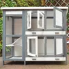 A multi-level outdoor pet enclosure with open doors and windows, set against a backdrop of greenery and a brick wall. Produktbild-Vorschau