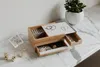 A wooden jewelry box with white accents sits on a marble countertop, next to a potted plant. Voir les images du produit