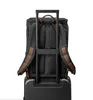The back of a black backpack with brown accents is shown attached to a black rolling suitcase. Produktbild-Vorschau