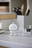 Two white Hoptimist figures on a desk with office supplies. Produktbild-Vorschau