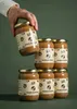 A hand is picking up a jar of hazelnut spread from a stack of jars. Produktbild-Vorschau
