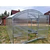 A polycarbonat greenhouse is set up in a grassy area with some trees and houses in the background. Produktbild-Vorschau