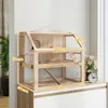 A wooden hamster cage with multiple levels and accessories, placed on a cabinet next to a plant and flowers. Náhled obrázku produktu