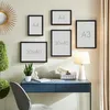A desk with a blue drawer unit, a chair, a lamp, and several framed pictures on the wall. Produktbild-Vorschau