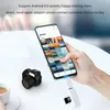 A hand holding a smartphone connected to a card reader, with a small camera and a cup of coffee on a table. Produktbild-Vorschau
