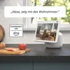 A smart display device is shown on a kitchen counter, displaying a video feed of a dog. A speech bubble indicates a voice command to Alexa. Produktbild-Vorschau