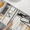 A person's hand is shown organizing a bathroom drawer filled with toiletries and beauty tools. Produktbild-Vorschau
