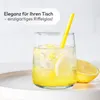 A glass of lemonade with ice and lemon slices, with a yellow straw, on a white tray, with a lemon half next to it. Produktbild-Vorschau