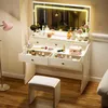 A white vanity table with a lighted mirror, drawers filled with makeup, and a stool in front. Produktbild-Vorschau