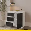 A white sideboard with black drawers and a black door, featuring a lamp and a bowl of fruit on top, placed in a room. Náhled obrázku produktu