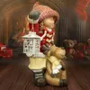 A Christmas-themed figurine of a girl holding a lantern and a reindeer, set against a cozy fireplace background with teddy bears and gift boxes. Produktbild-Vorschau