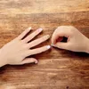 A close-up shot of two hands on a wooden surface, one hand with decorated nails and the other applying a nail sticker. Anteprima dell’immagine prodotto