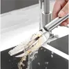 A hand is holding a stainless steel fish scaler under a running faucet in a kitchen sink. Náhled obrázku produktu