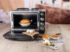 A kitchen appliance on a wooden table with food in the oven and on the side. Produktbild-Vorschau