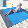 A woman in a bikini and hat is relaxing on a blue and gray beach blanket on a sandy beach. Produktbild-Vorschau