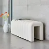 A white bench with a fluted design sits in a modern interior with a concrete wall and floor. A vase with orange flowers is placed next to the bench. Anteprima dell’immagine prodotto