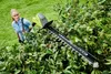 A woman is using a hedge trimmer to trim a large bush. Produktbild-Vorschau