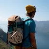 Person mit gelber Mütze und blauer T-Shirt; trägt Rucksack mit Klettergriff "Penta" von YY Vertical; steht an einem Aussichtspunkt. Podgląd zdjęcia produktu